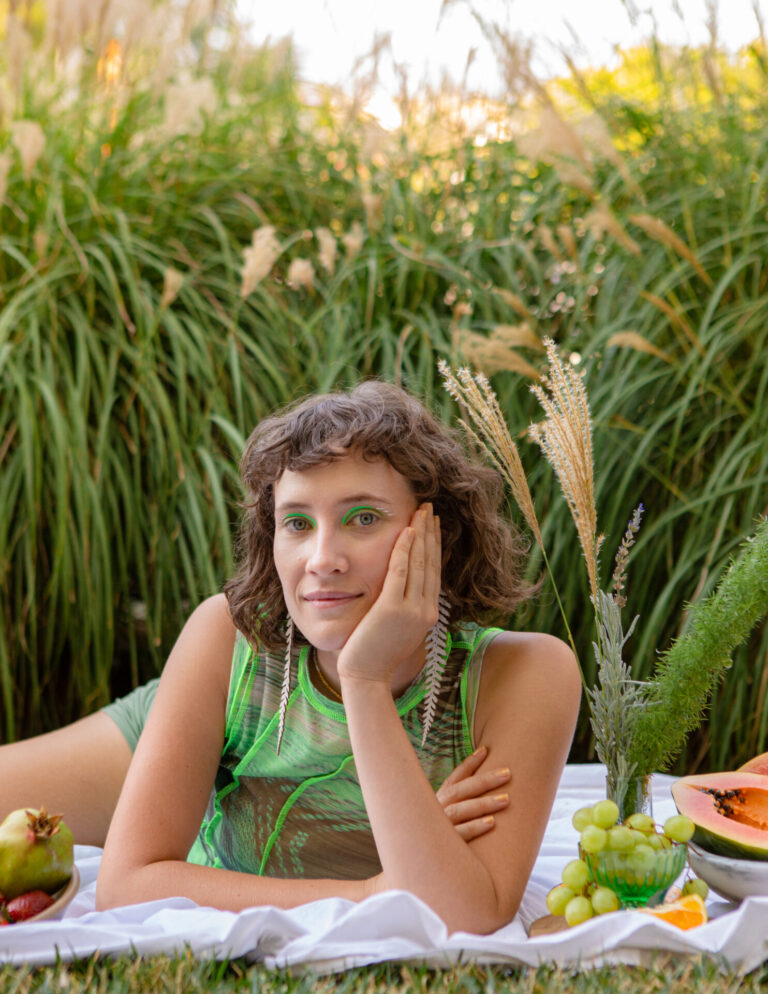 Euphemia Russell is wearing lime green sitting in a wheat field with a picnic of grapes, pawpaw, orange and strawberry